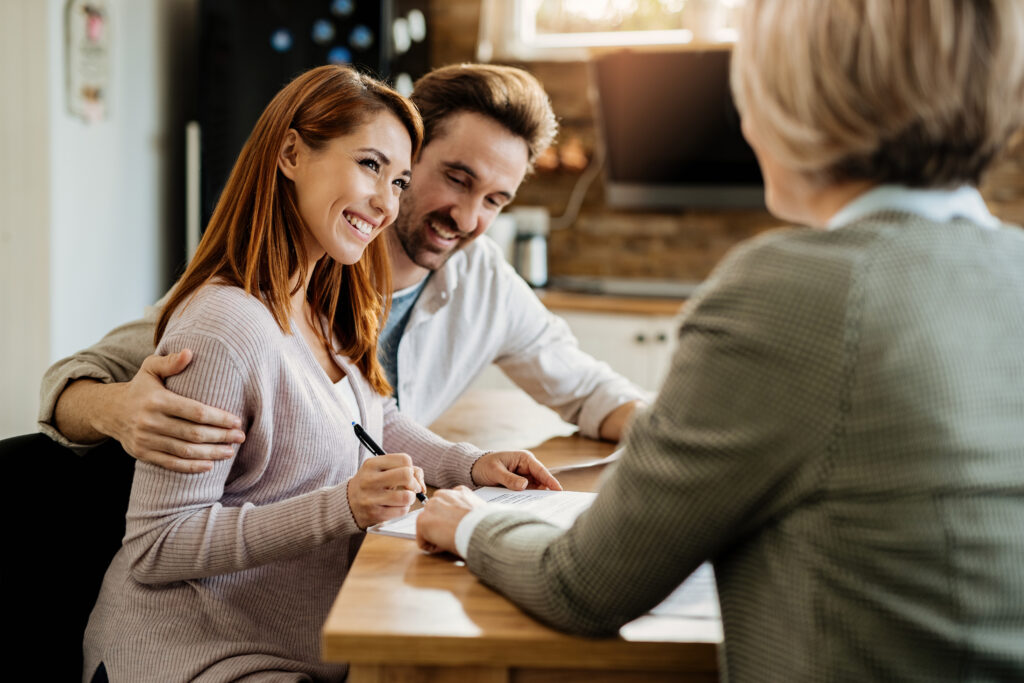 young-happy-woman-her-husband-signing-agreement-with-home-agent-during-meeting-scaled.